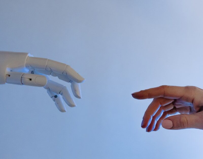 humand hand raching for robot hand to illustrate ai technology