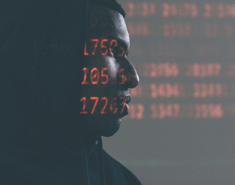 suspicious person with computercode symbolizing cybercrime and hacking